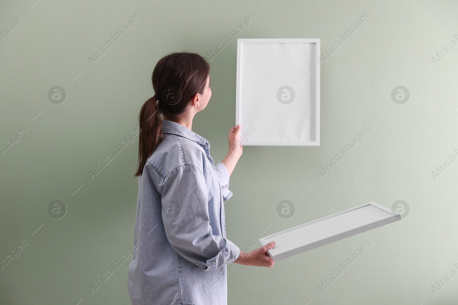 Woman hanging blank frames on green wall, back view Photo of Woman hanging blank frames on green wall, back view