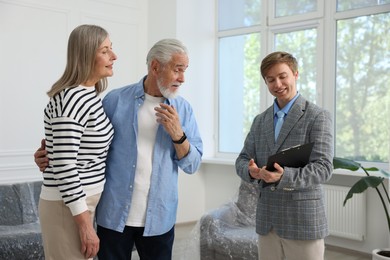 Photo of Smiling real estate agent with clipboard working with couple at home