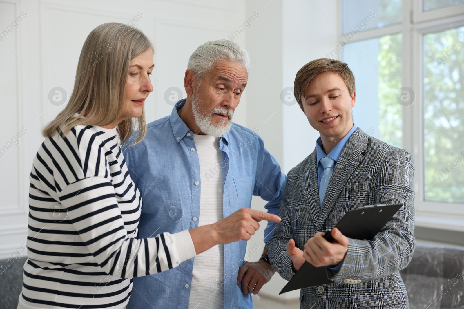 Smiling real estate agent with clipboard working with couple at home Photo of Smiling real estate agent with clipboard working with couple at home