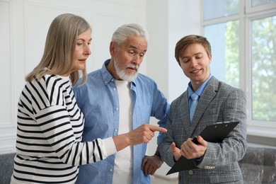 Photo of Smiling real estate agent with clipboard working with couple at home