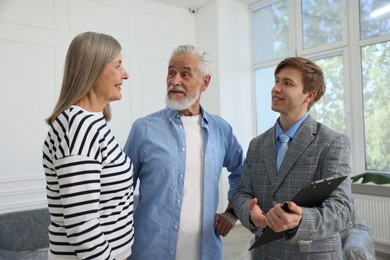 Photo of Smiling real estate agent with clipboard working with couple at home