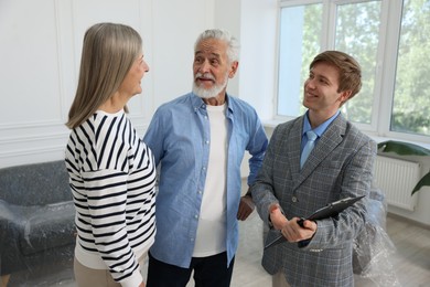 Photo of Smiling real estate agent with clipboard working with couple at home