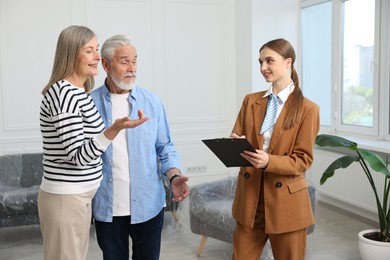 Photo of Smiling real estate agent with clipboard working with couple at home