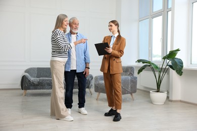 Photo of Smiling real estate agent with clipboard working with couple at home