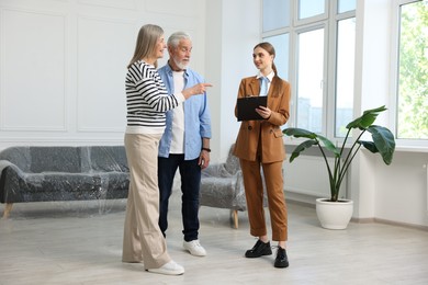 Photo of Smiling real estate agent with clipboard working with couple at home