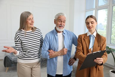 Photo of Smiling real estate agent with clipboard working with couple at home