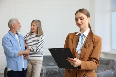 Photo of Smiling real estate agent with clipboard and couple at home, selective focus