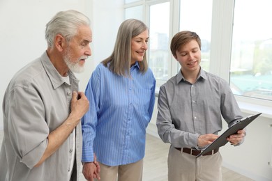 Photo of Smiling real estate agent with clipboard working with couple at home