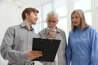Photo of Smiling real estate agent with clipboard working with couple at home, low angle view