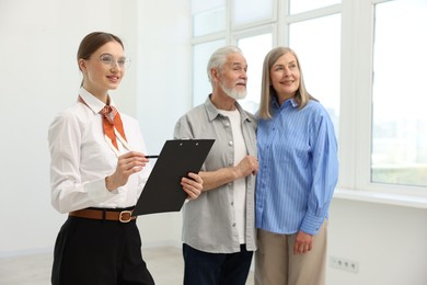 Photo of Smiling real estate agent with clipboard and couple at home