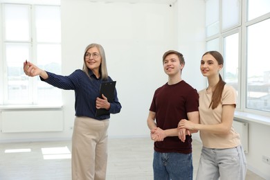 Photo of Smiling real estate agent showing apartment to couple indoors.