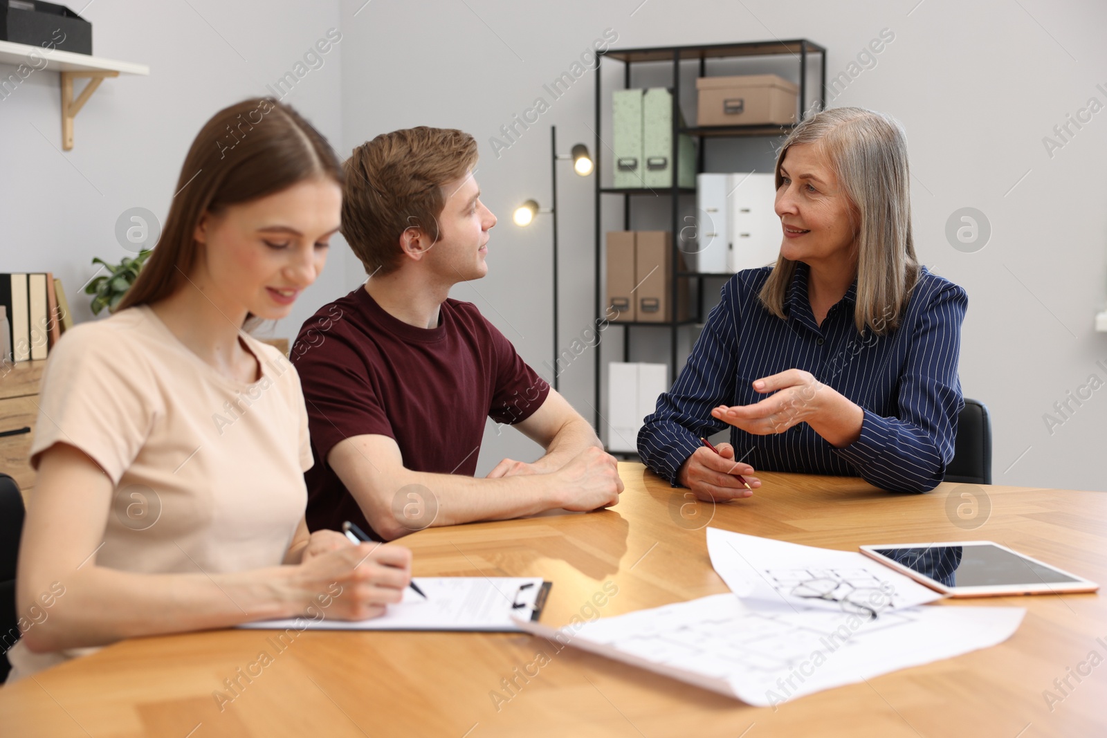 Smiling real estate agent working with couple at table in office Photo of Smiling real estate agent working with couple at table in office