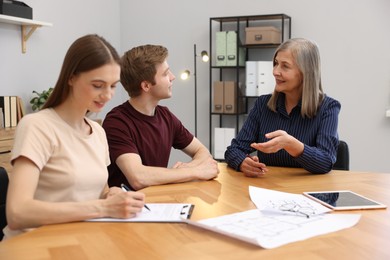 Photo of Smiling real estate agent working with couple at table in office