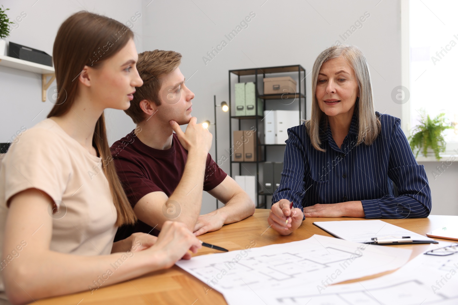 Smiling real estate agent working with couple at table in office Photo of Smiling real estate agent working with couple at table in office
