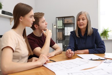 Photo of Smiling real estate agent working with couple at table in office