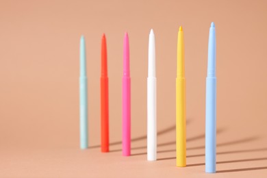 Photo of Colorful twist up eye pencils on beige background, closeup