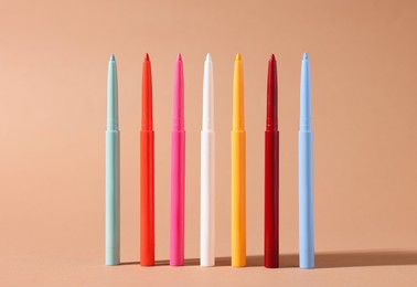 Photo of Colorful twist up eye pencils on beige background, closeup
