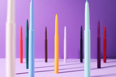 Photo of Colorful twist up eye pencils on purple background, selective focus