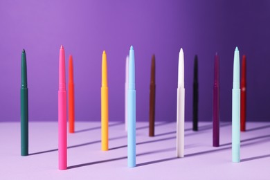 Photo of Colorful twist up eye pencils on purple background, closeup