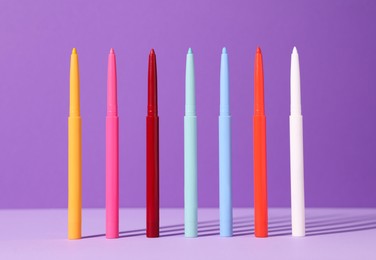 Photo of Colorful twist up eye pencils on purple background, closeup