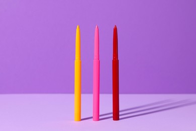 Photo of Colorful twist up eye pencils on purple background, closeup