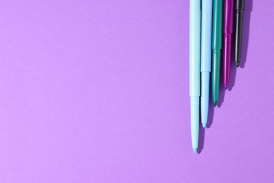 Photo of Colorful twist up eye pencils on purple background, flat lay. Space for text