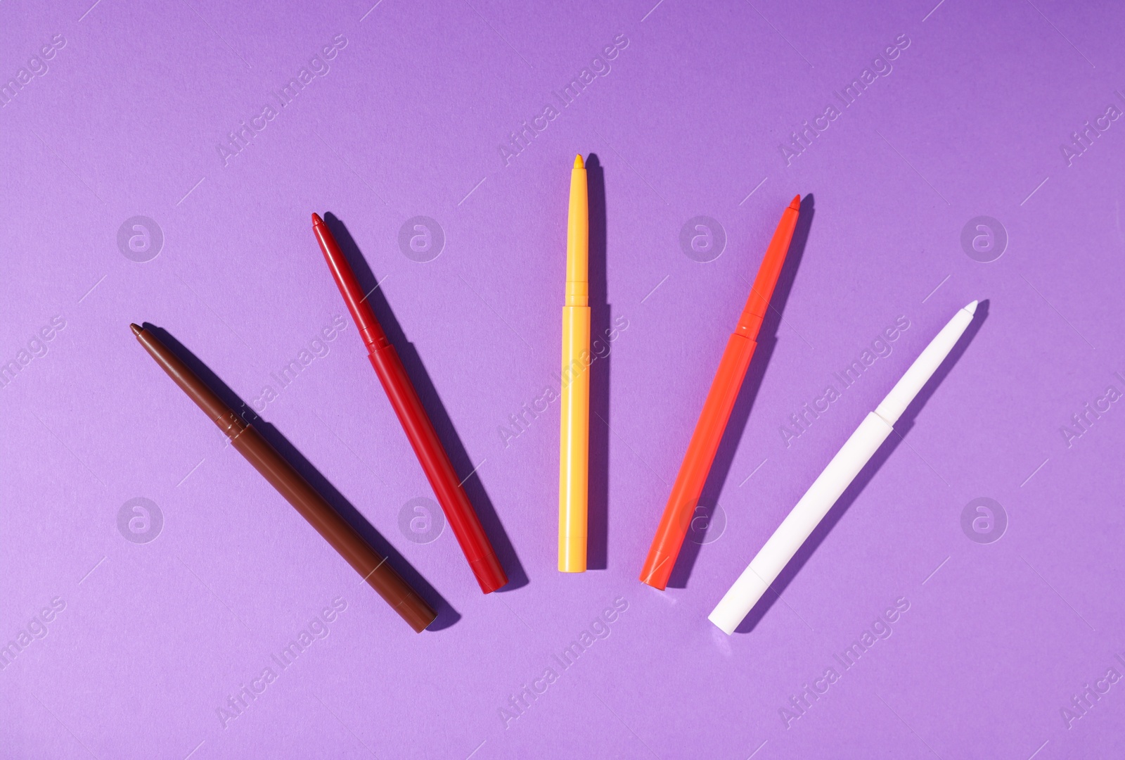 Colorful twist up eye pencils on purple background, flat lay Photo of Colorful twist up eye pencils on purple background, flat lay