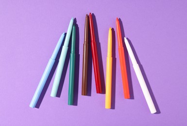 Photo of Colorful twist up eye pencils on purple background, flat lay