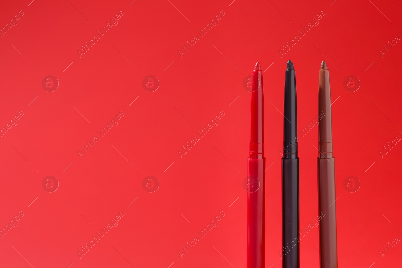 Colorful twist up eye pencils on red background, closeup. Space for text Photo of Colorful twist up eye pencils on red background, closeup. Space for text