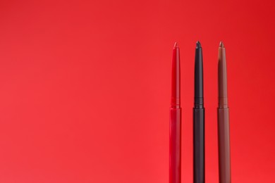 Photo of Colorful twist up eye pencils on red background, closeup. Space for text
