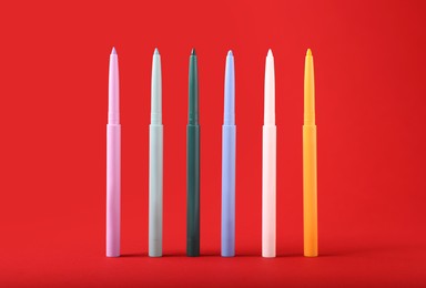 Photo of Colorful twist up eye pencils on red background, closeup