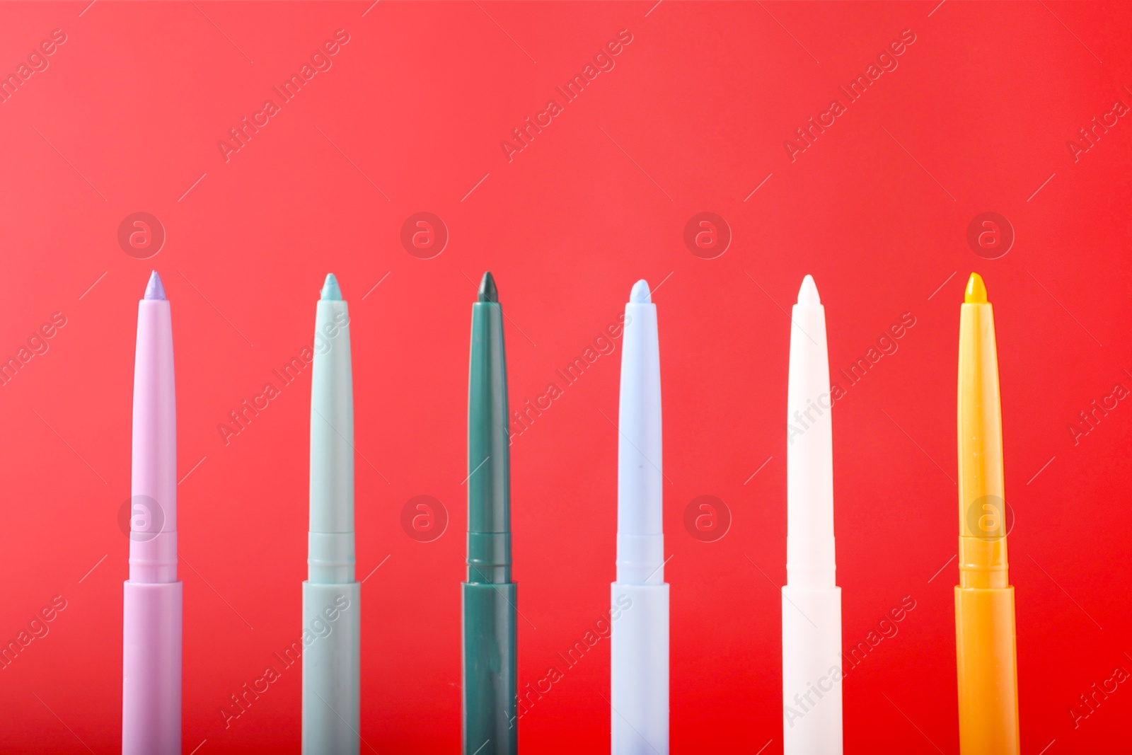 Colorful twist up eye pencils on red background, closeup Photo of Colorful twist up eye pencils on red background, closeup