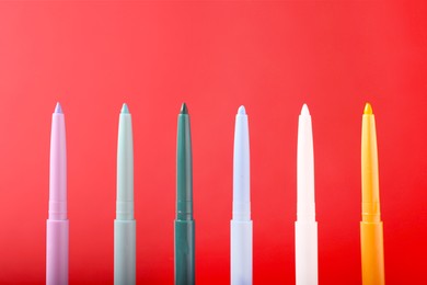 Photo of Colorful twist up eye pencils on red background, closeup