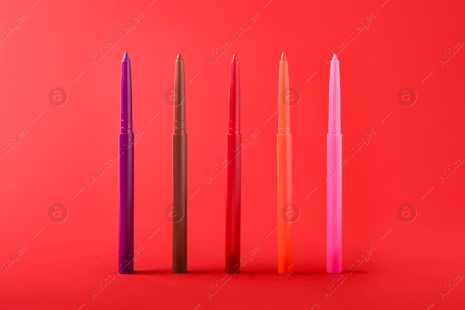 Colorful twist up eye pencils on red background, closeup Photo of Colorful twist up eye pencils on red background, closeup