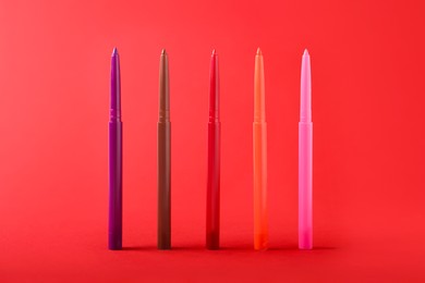 Photo of Colorful twist up eye pencils on red background, closeup