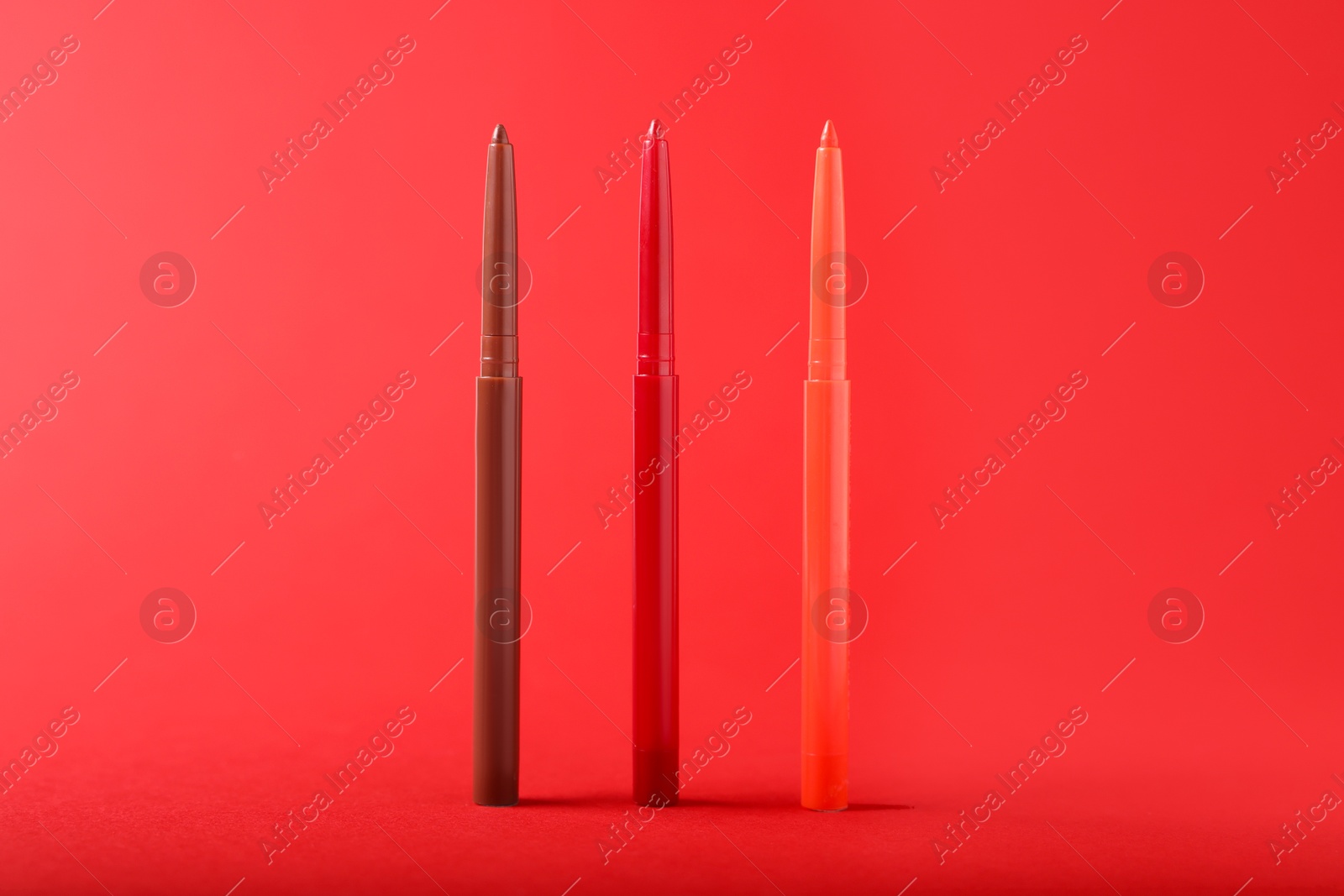 Colorful twist up eye pencils on red background, closeup Photo of Colorful twist up eye pencils on red background, closeup