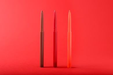 Photo of Colorful twist up eye pencils on red background, closeup
