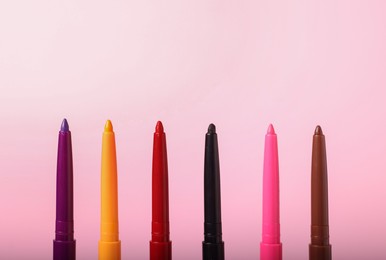 Photo of Colorful twist up eye pencils on pink background, closeup