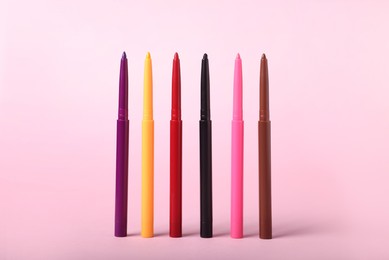 Photo of Colorful twist up eye pencils on pink background, closeup