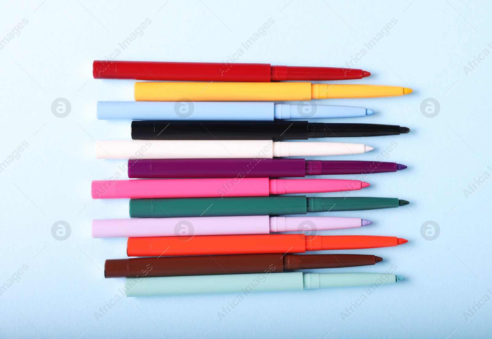 Colorful twist up eye pencils on light blue background, flat lay Photo of Colorful twist up eye pencils on light blue background, flat lay