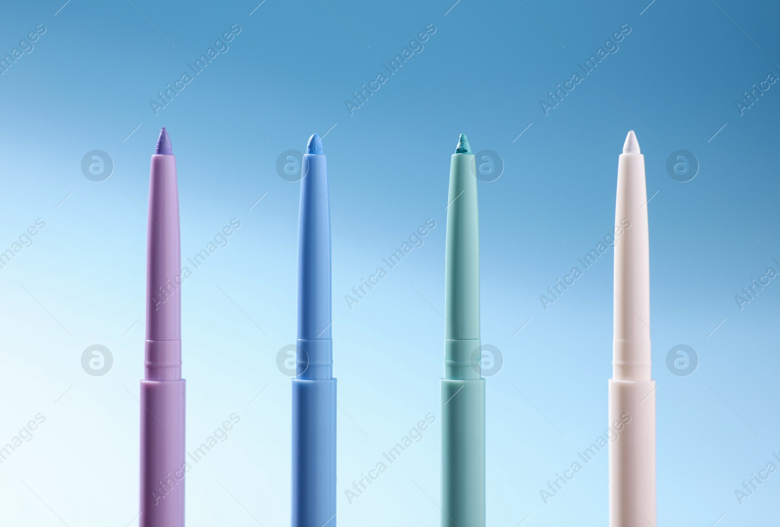 Colorful twist up eye pencils on light blue gradient background, closeup Photo of Colorful twist up eye pencils on light blue gradient background, closeup
