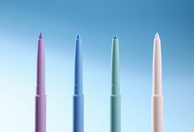 Photo of Colorful twist up eye pencils on light blue gradient background, closeup