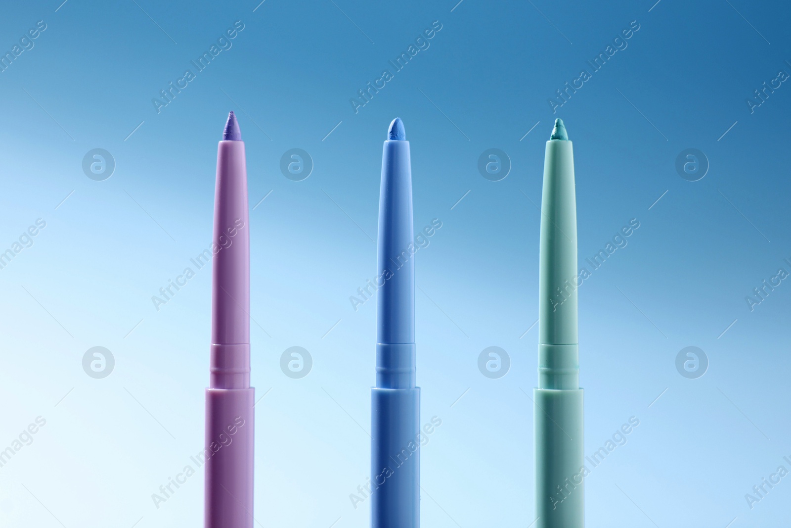 Colorful twist up eye pencils on light blue gradient background, closeup Photo of Colorful twist up eye pencils on light blue gradient background, closeup