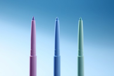 Photo of Colorful twist up eye pencils on light blue gradient background, closeup