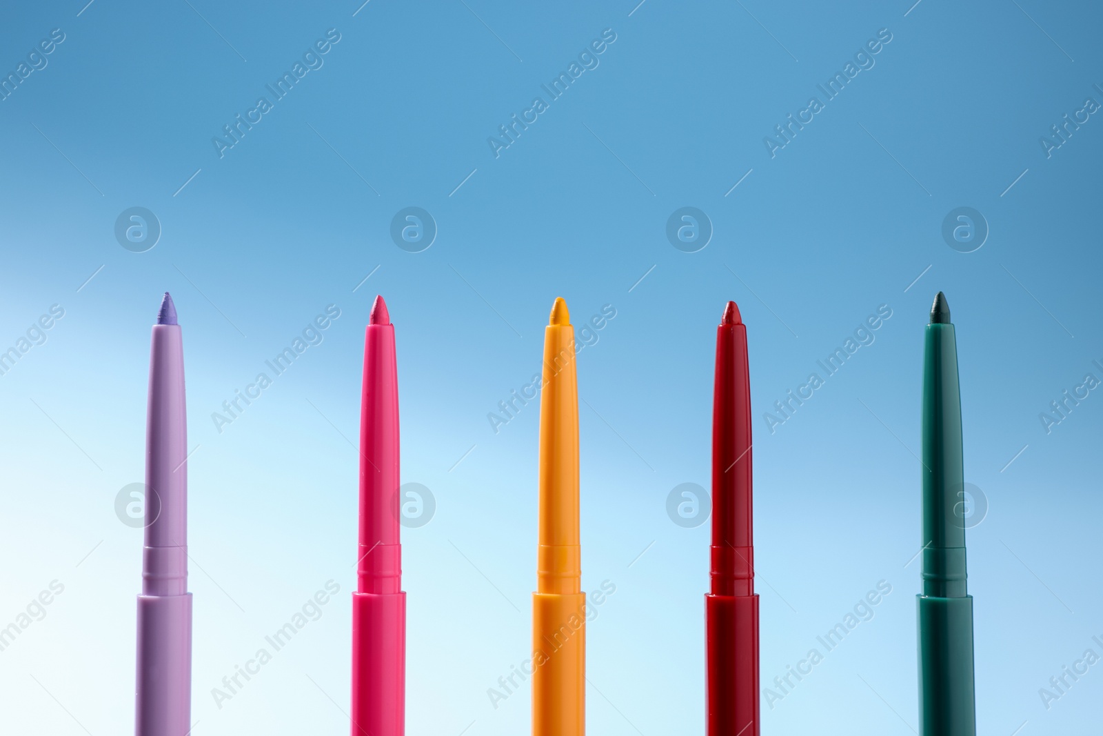 Colorful twist up eye pencils on light blue gradient background, closeup Photo of Colorful twist up eye pencils on light blue gradient background, closeup