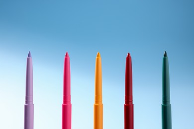 Photo of Colorful twist up eye pencils on light blue gradient background, closeup
