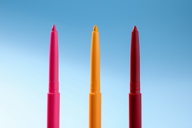 Photo of Colorful twist up eye pencils on light blue gradient background, closeup