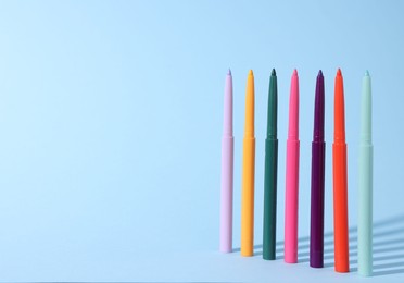 Photo of Colorful twist up eye pencils on light blue background. Space for text