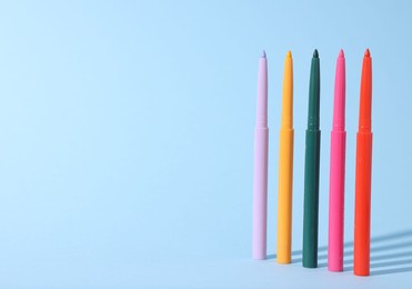 Photo of Colorful twist up eye pencils on light blue background. Space for text