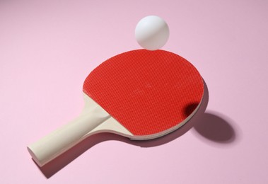 Photo of Ping pong racket and ball on pink background, closeup